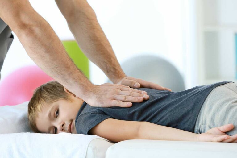 Adult receiving a gentle spinal mobility assessment while reviewing exercises with a clinician in a bright office.